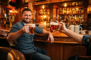Two male friends drinks beer at the counter in pub